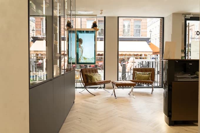 Bright clinic reception area with a herringbone wooden floor, leather lounge chairs and large street-facing windows