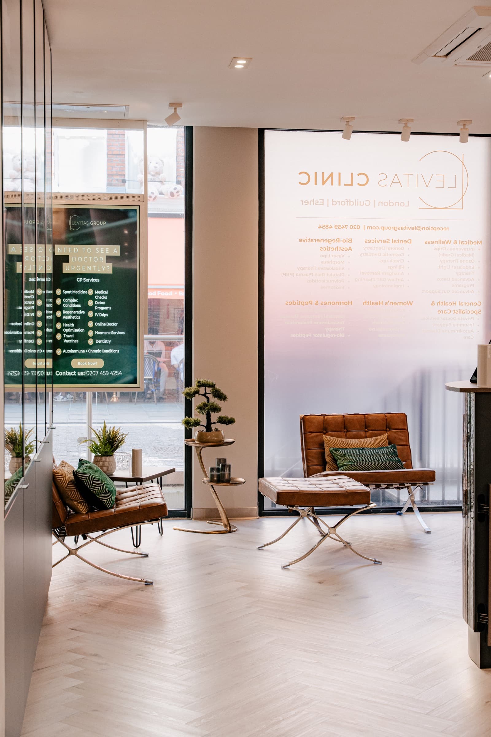 Seating area inside a Levitas clinic with leather chairs on a herringbone floor beside a glass wall
