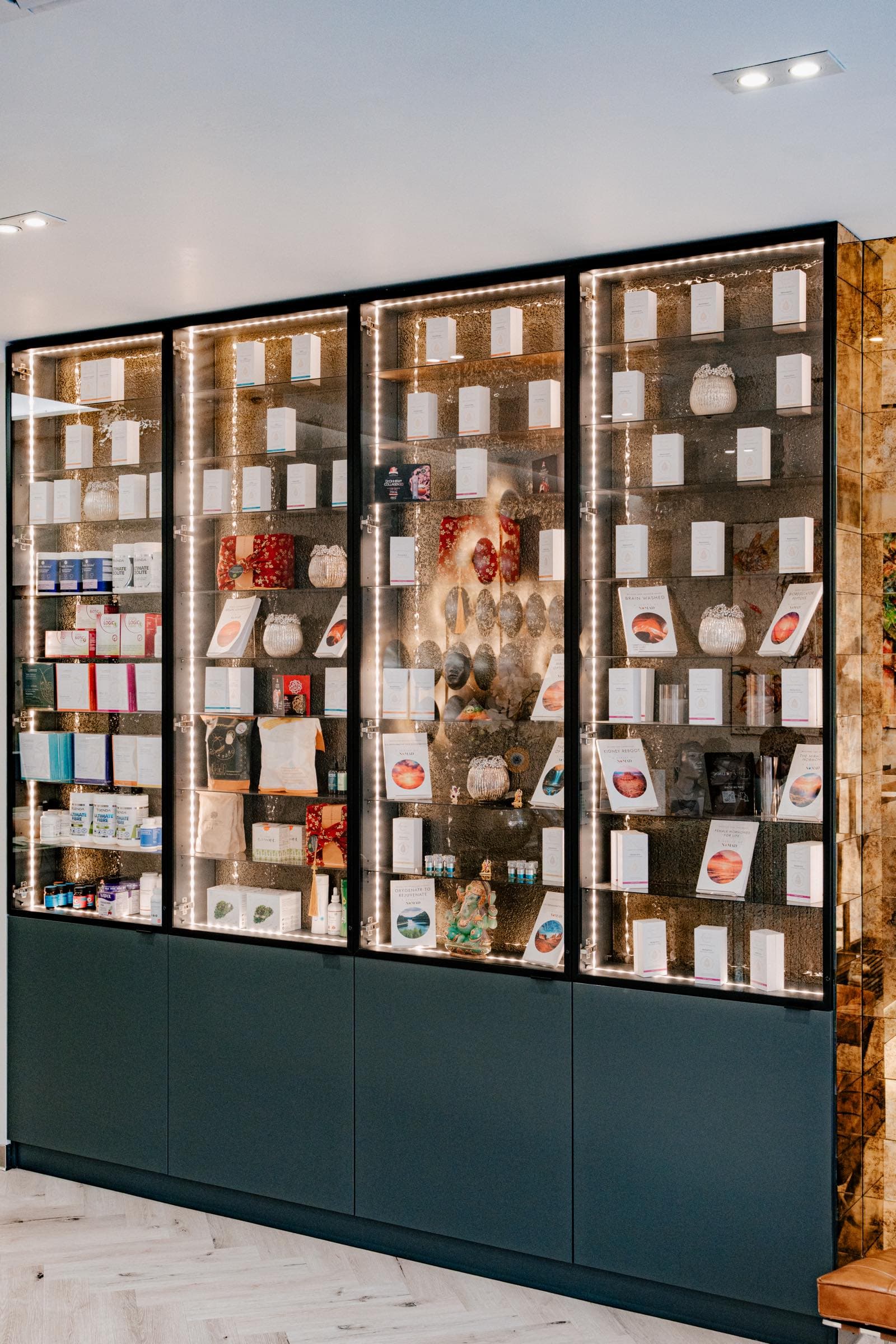 Backlit glass display cabinets in a Levitas clinic stocked with supplements, skincare and NOMAD books