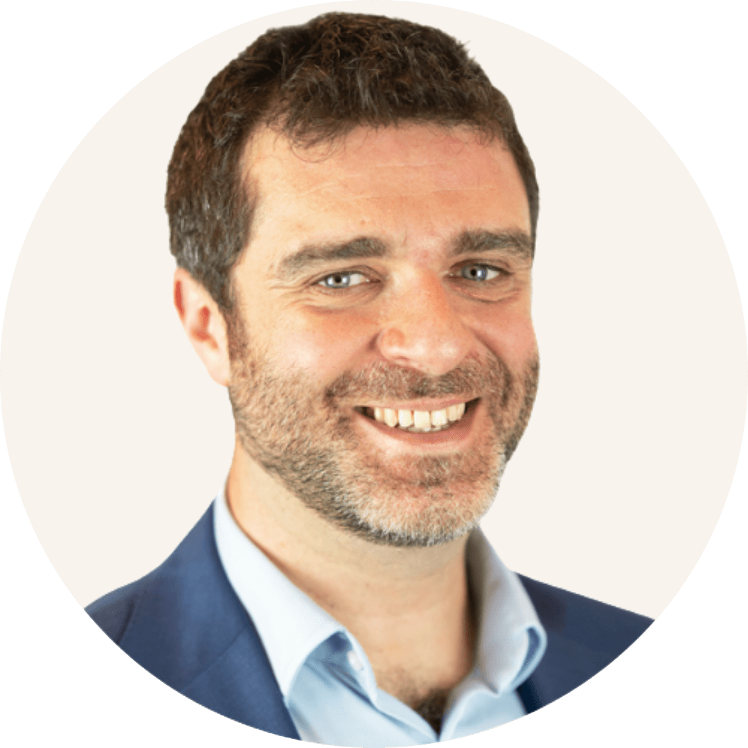Dr David Rigby smiling, with short curly brown hair and stubble, wearing a navy blazer and a light blue shirt