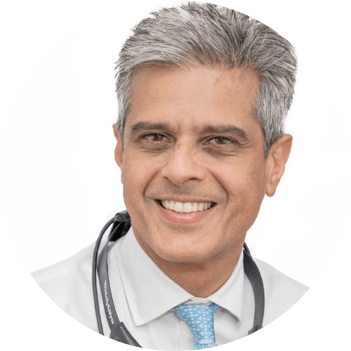Hamid Daya smiling, with grey hair, wearing a white shirt, a light blue tie and a stethoscope