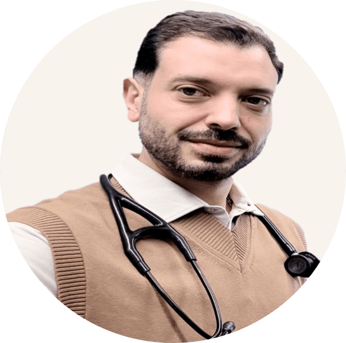 Dr Moe Irshidat, with dark hair and a beard, wearing a camel tank top over a white collared shirt, a stethoscope around his neck