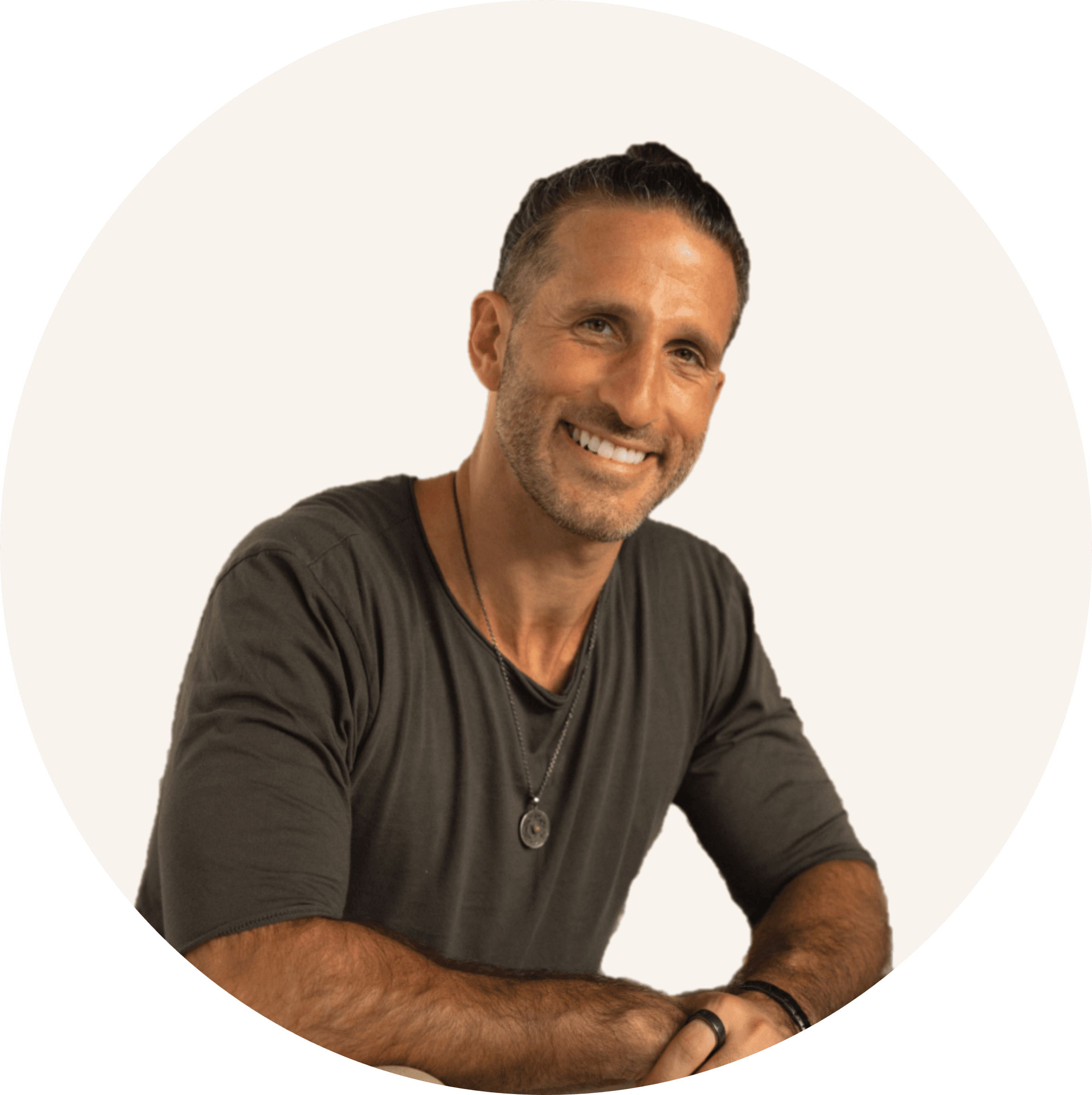Salim Najjar smiling, with dark hair tied back, wearing a dark grey T-shirt and a pendant necklace